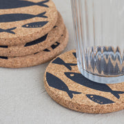 Cork coaster with grey fish design on table with glass on one